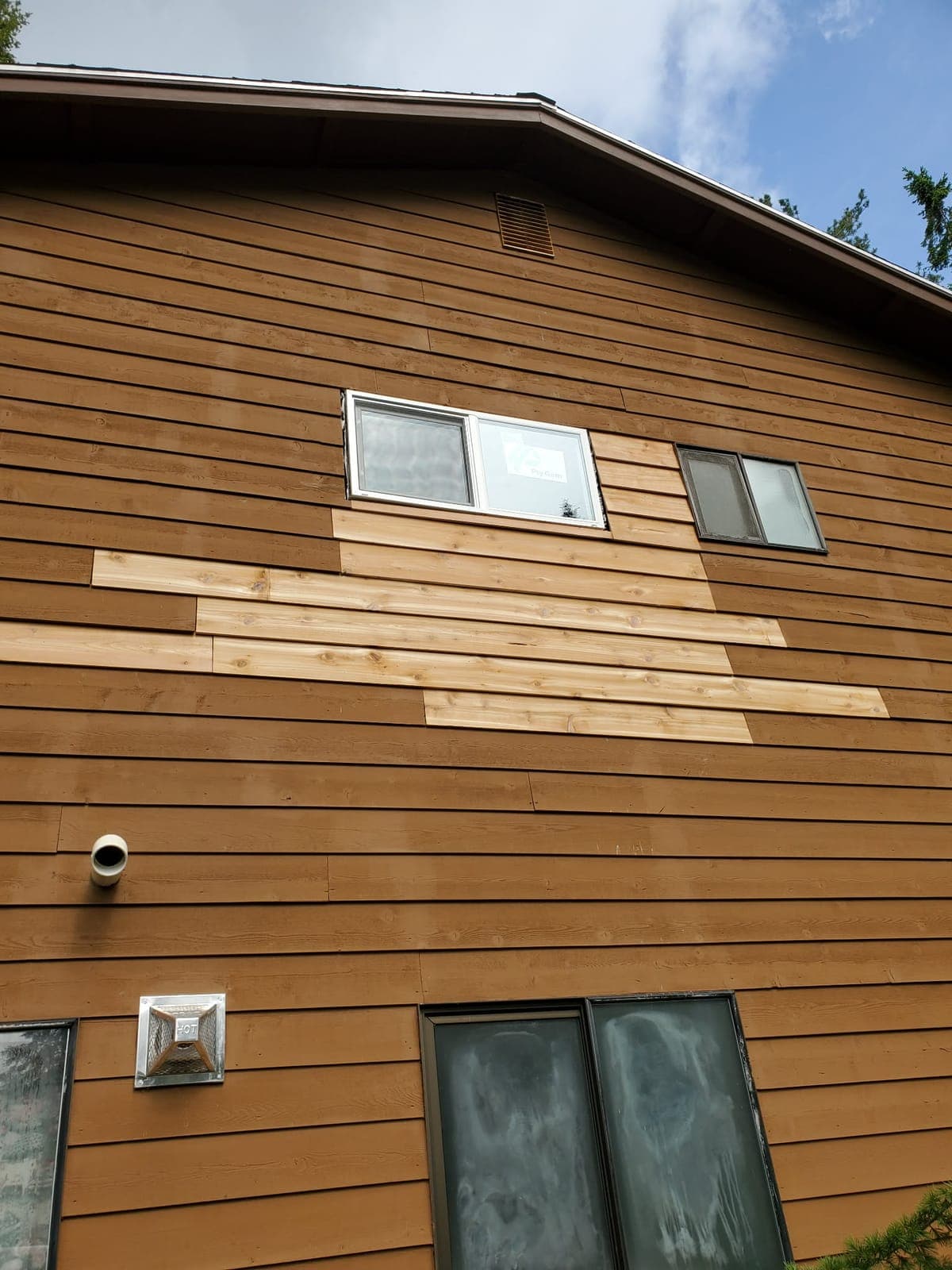 Stained cedar lap siding wall with new replacement boards fitted in around the windows