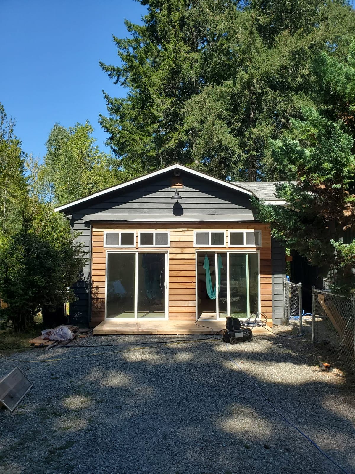 Home exterior with new cedar siding, sliding glass doors below transom windows, and a small deck landing, surrounded by evergreens
