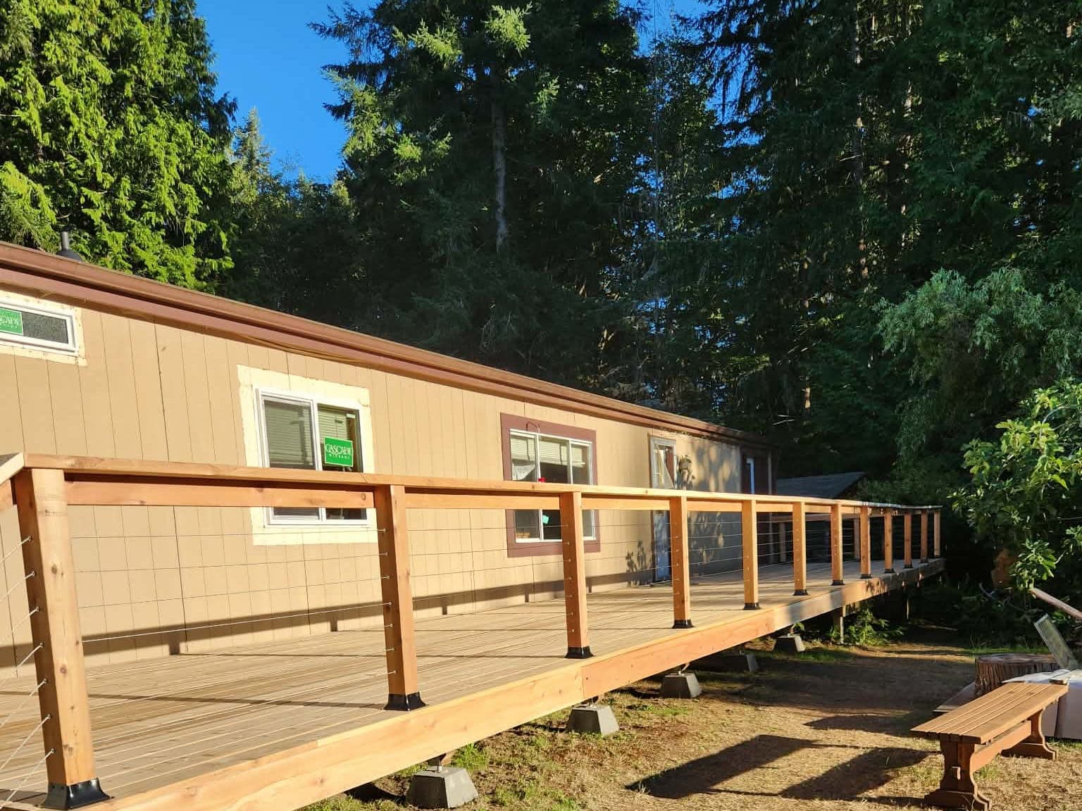 Full-length cedar deck with stainless cable railing running along a home, backed by evergreens in late afternoon light